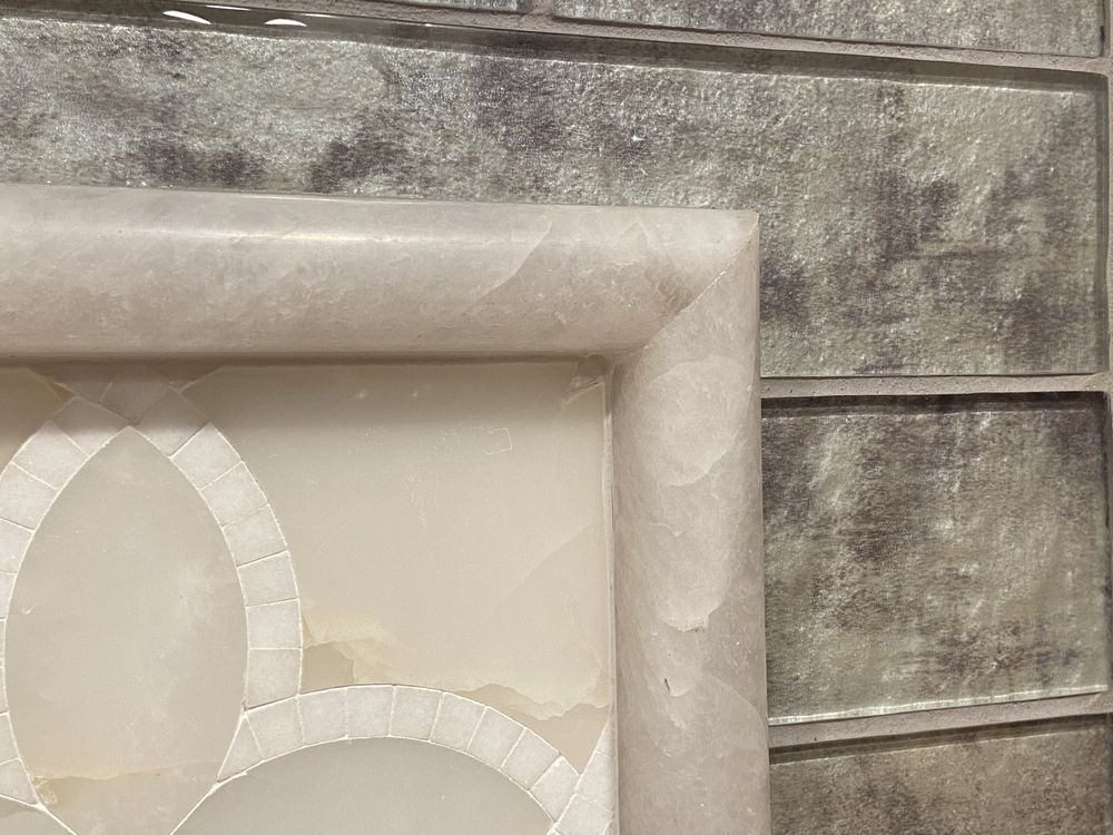 Close-up of a white marble frame against a textured gray tile wall.