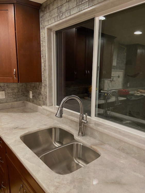 Kitchen with double sink, faucet, and window above. Light countertops, dark cabinets, and backsplash.