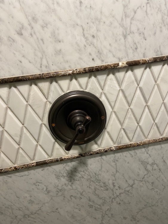 Dark bronze shower valve on white diamond-patterned tiles, set within marble.