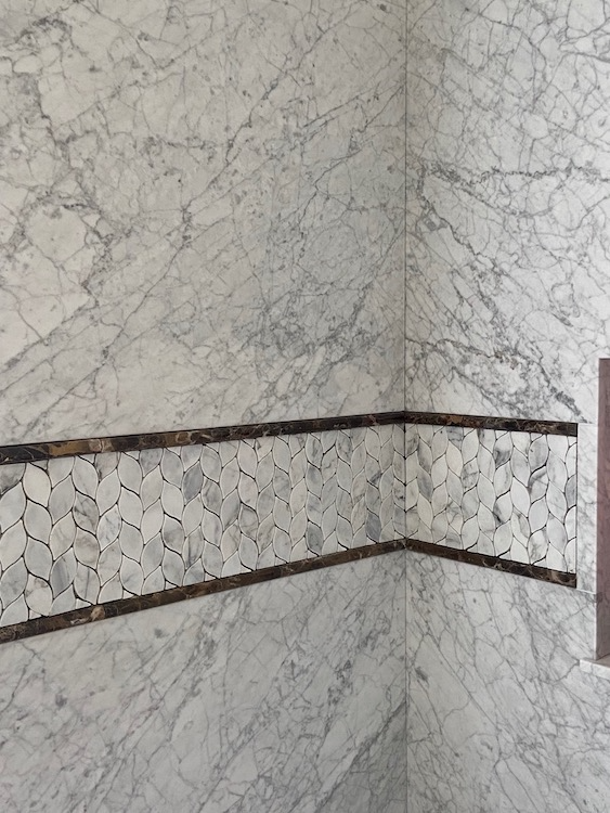 Marble tiled shower with decorative mosaic border.