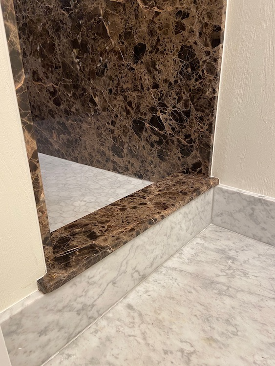 Brown and tan marble wall and step leading to a light marble floor.