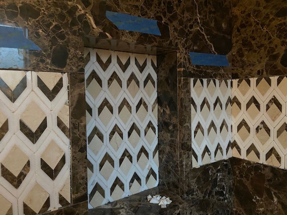 Tiles being installed on a wall; patterned cream and beige geometric design against dark brown marble.