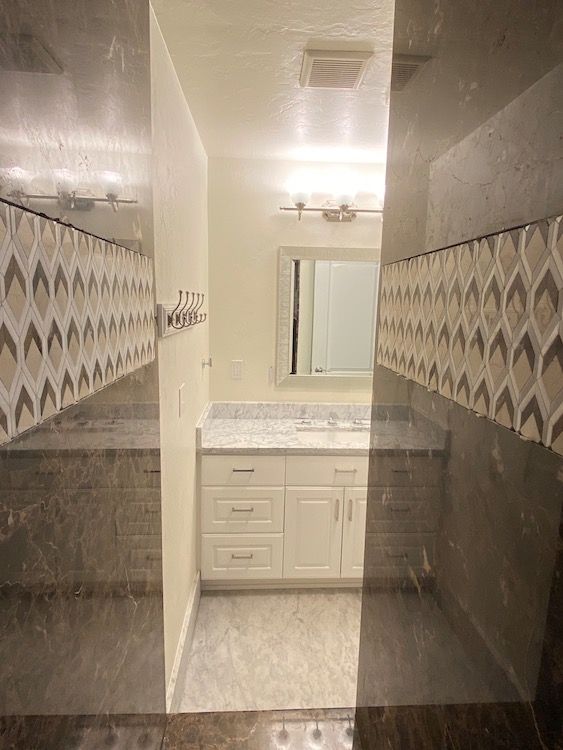 Bathroom with white vanity, gray countertops, and tiled walls with decorative accents.