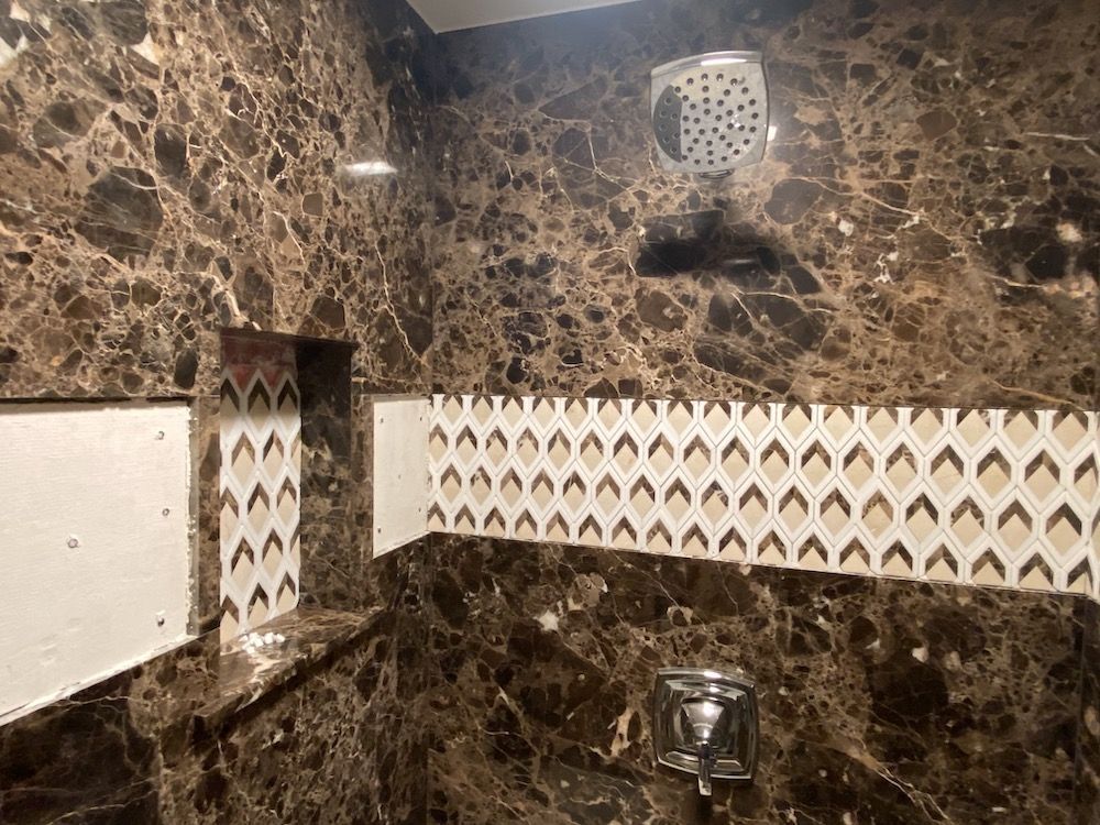 Dark brown marble-tiled shower with a decorative border and a silver showerhead and faucet.