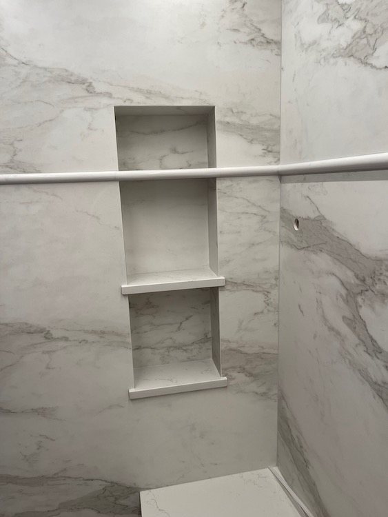 White marble-tiled shower with built-in shelf and a white rod.