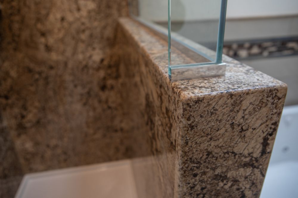 Close-up of granite bathroom ledge with glass shower door, highlighting texture and materials.