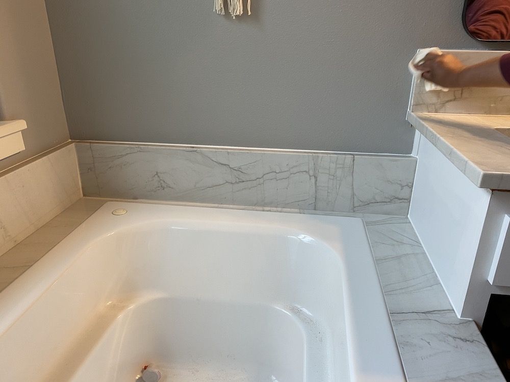 White bathtub, marble tiles, gray wall, hand wiping countertop.