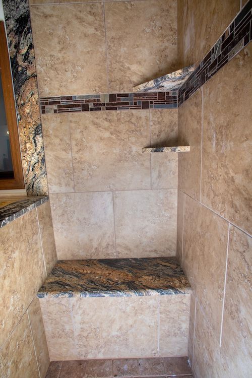Shower with brown tile, a granite bench, and built-in shelves.