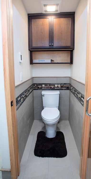 Small bathroom with a toilet, dark brown cabinet, and a decorative tile border.