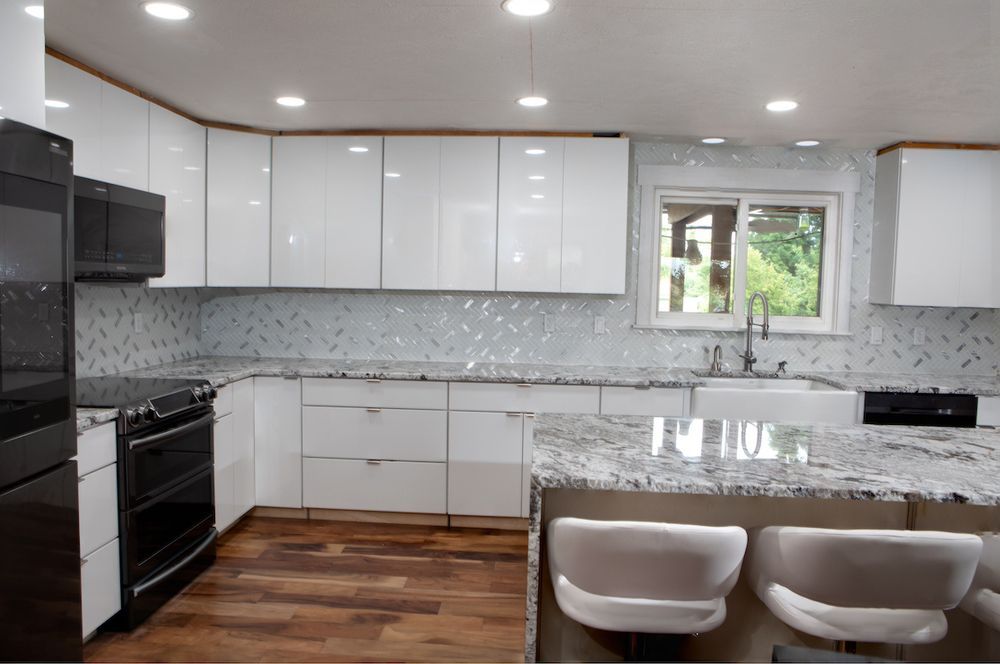 Modern white kitchen with granite countertops, stainless steel appliances, and wood flooring.