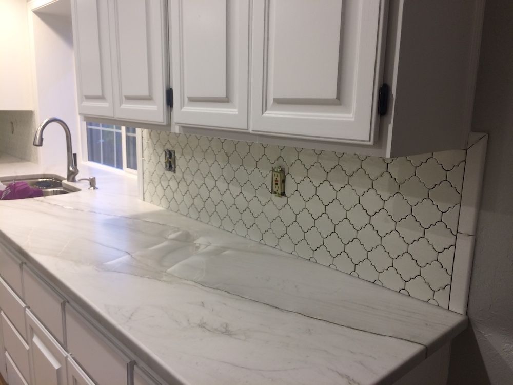 White kitchen with white cabinets, countertop, and patterned tile backsplash.