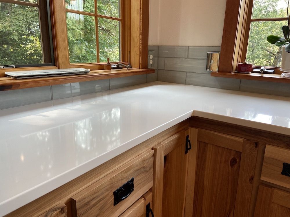 White countertop in a kitchen with wooden cabinets and windows.
