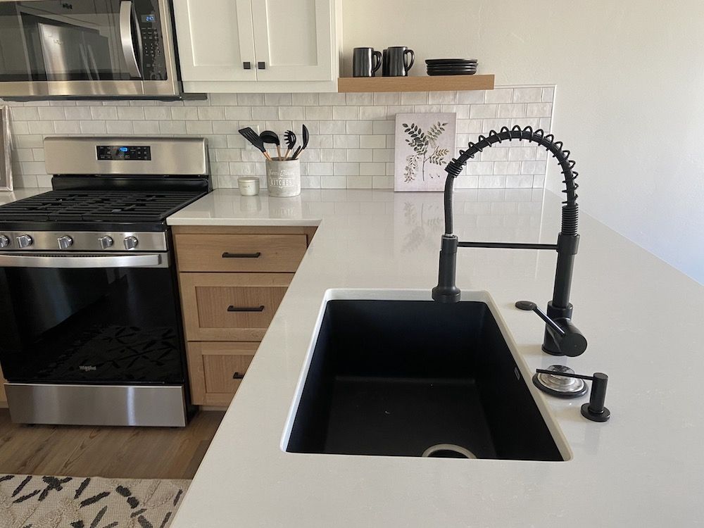 Kitchen with black sink, faucet, stainless steel appliances, white countertop, and white subway tile backsplash.