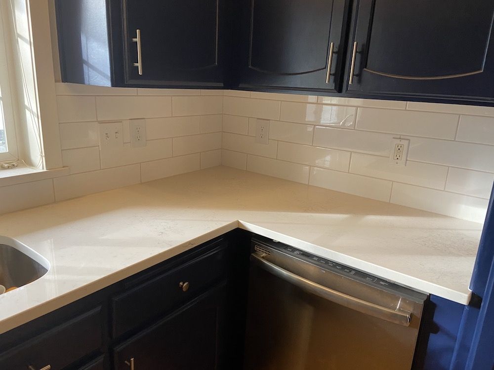 Kitchen corner with navy cabinets, white countertops, and white subway tile backsplash.