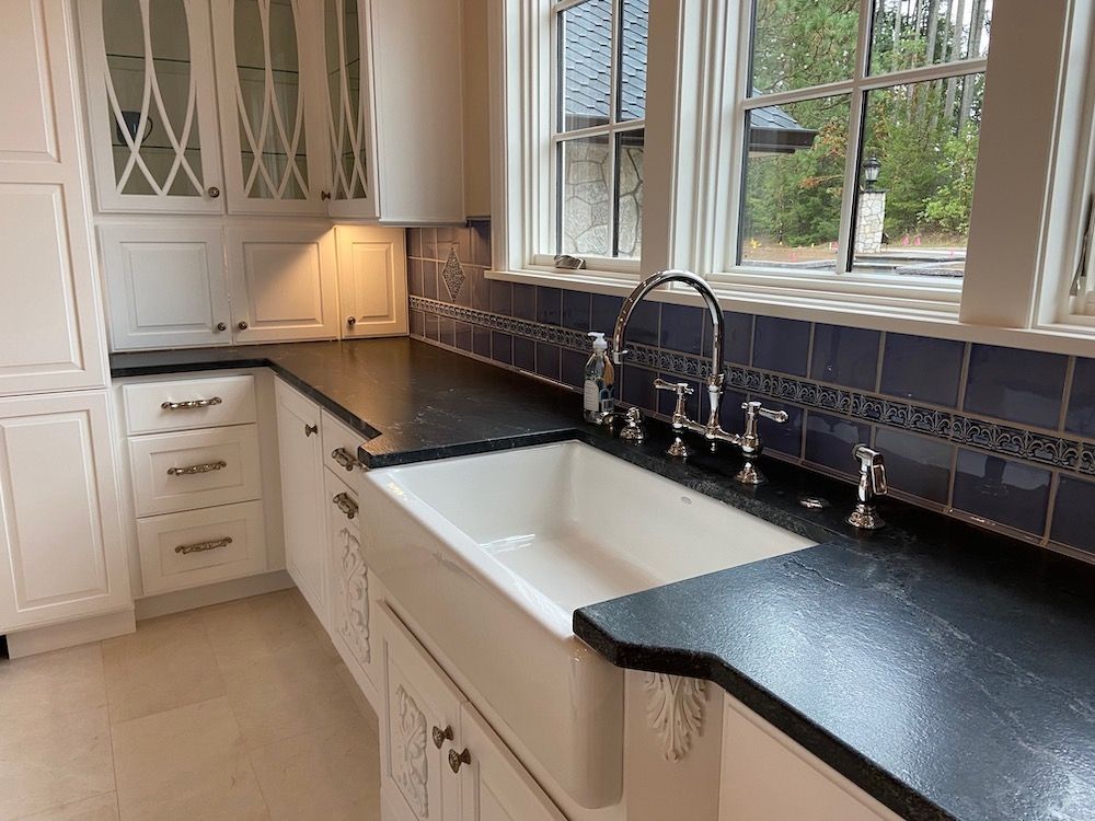 Kitchen with white cabinets, dark countertops, farmhouse sink, and window.