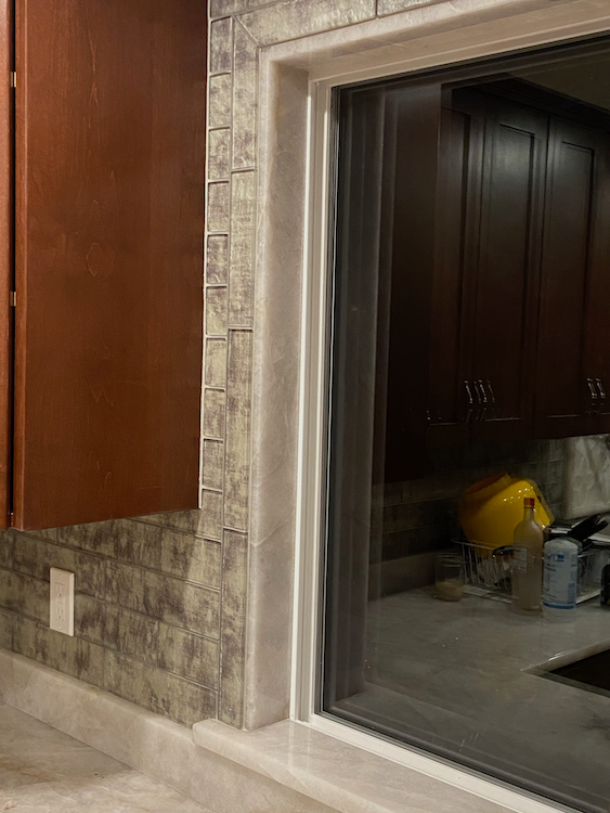 Window frame with stone veneer and dark cabinetry visible through glass.