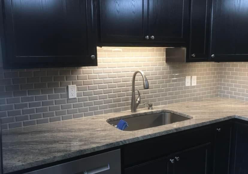 Kitchen with dark cabinets, gray backsplash, and stainless steel sink.