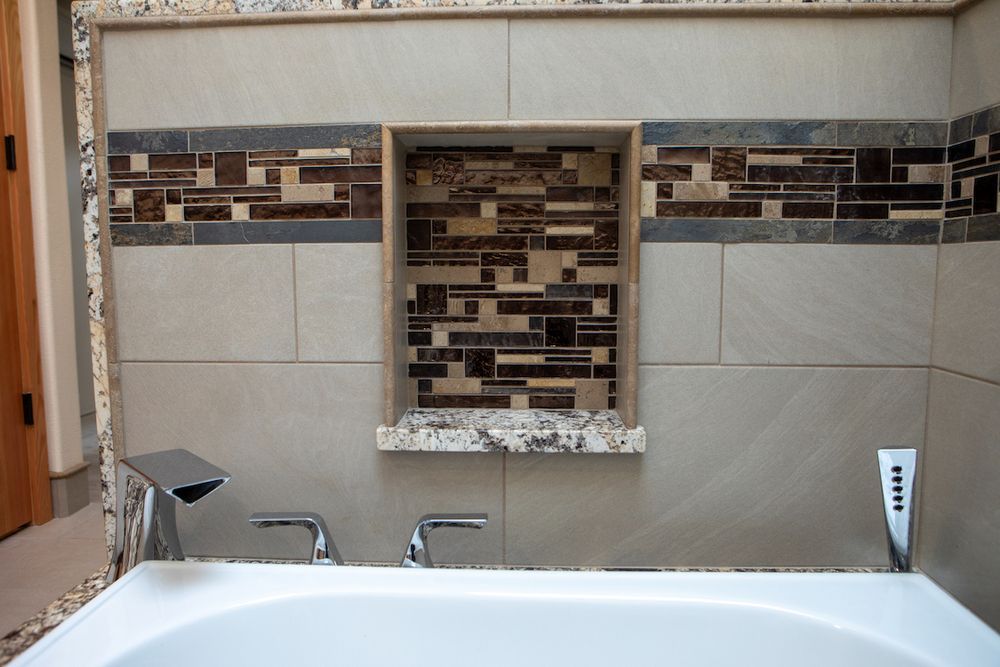 Bathroom with tiled wall, built-in shelf, and bathtub faucet. The shelf has mosaic tile.