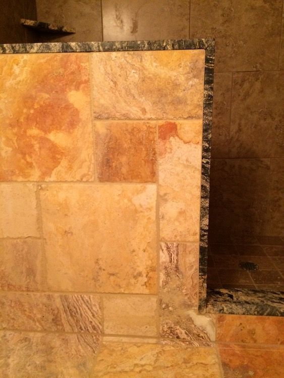 Shower with beige and tan stone tile, dark border, and marble base.