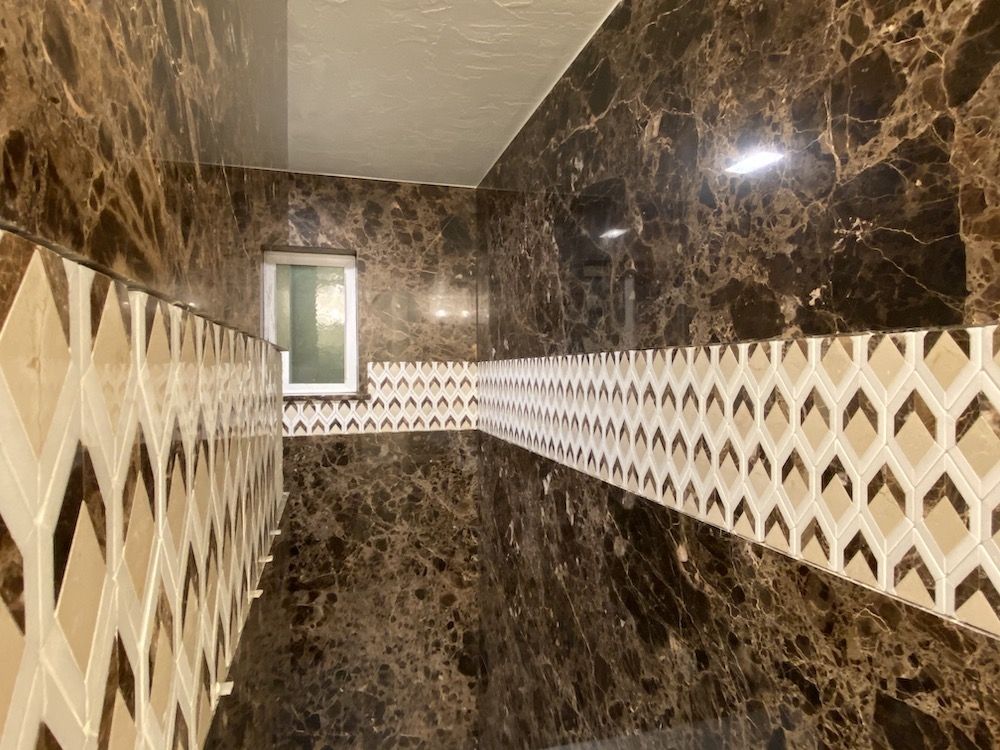 Brown marble tiled walls with a patterned tile border and a small window.