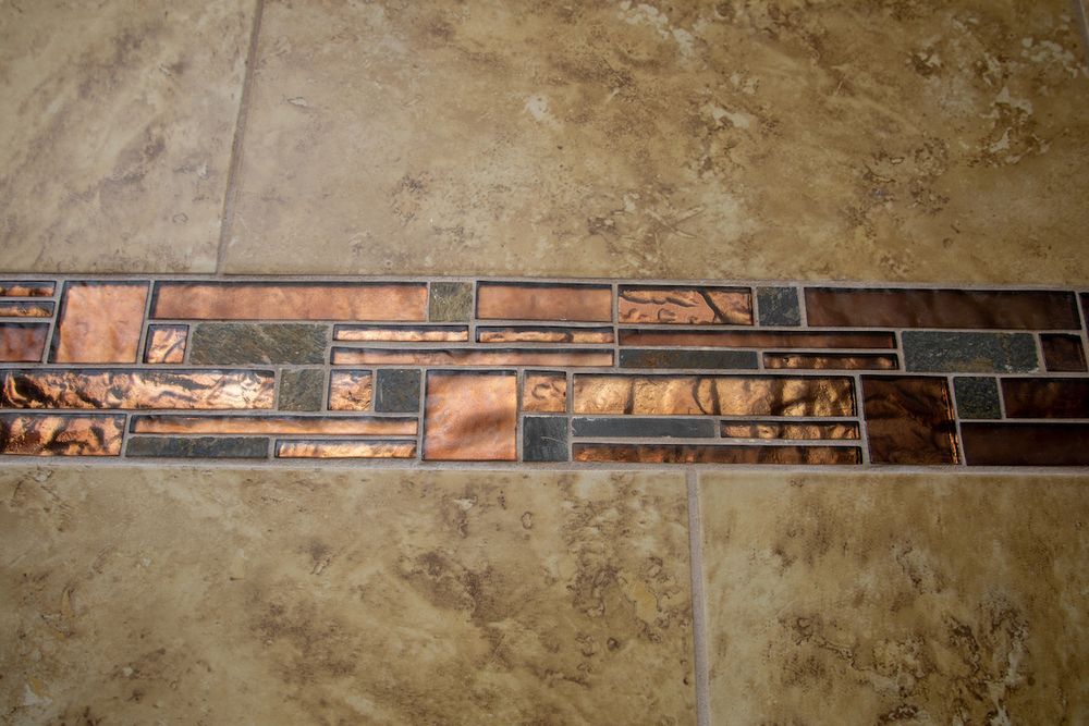Beige tiled floor with a mosaic border of copper and dark green tiles.