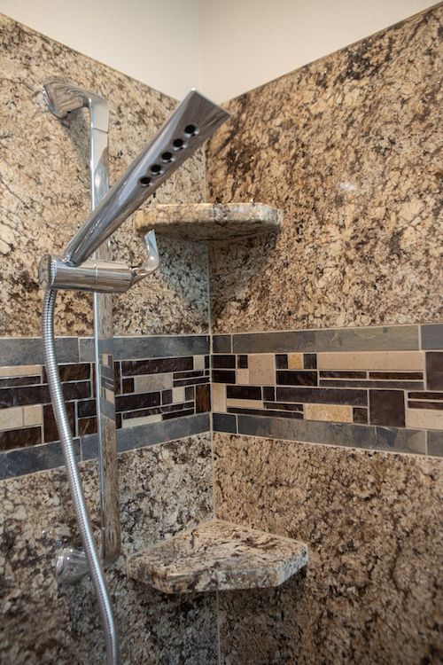 Shower with granite walls, decorative tile border, chrome showerhead, and corner shelves.
