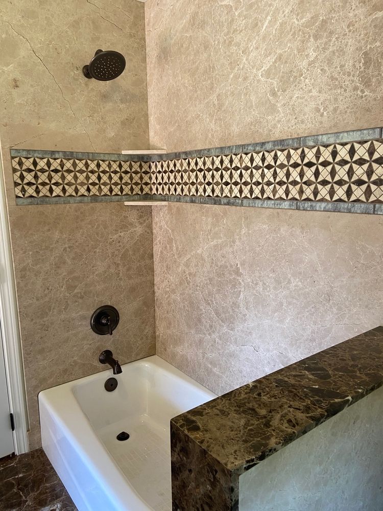 Bathroom with brown tile walls, decorative border, white tub, and dark bronze fixtures.