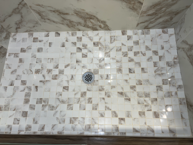 Shower floor tiled in a square mosaic pattern of white and brown, with a central drain.