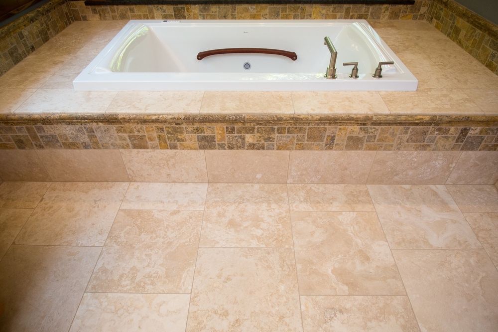 A built-in white bathtub surrounded by tan tile and a mosaic tile border.