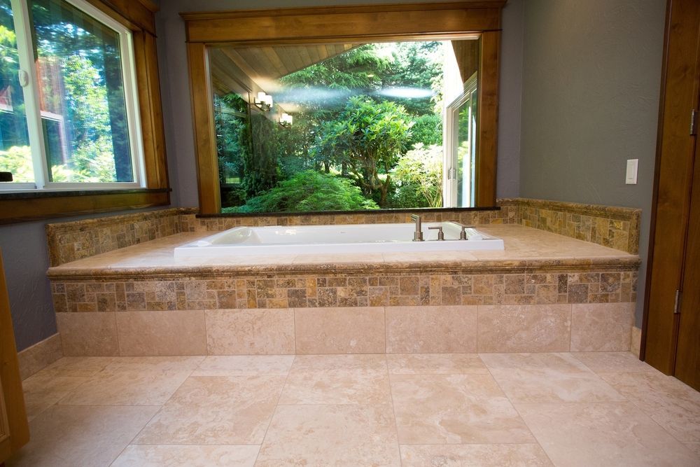 Bathroom with a built-in tub, beige tile, and a large window overlooking trees.