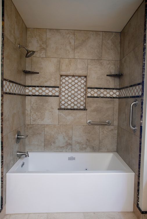 Bathroom with tan tile, white tub, showerhead, and grab bars for accessibility.
