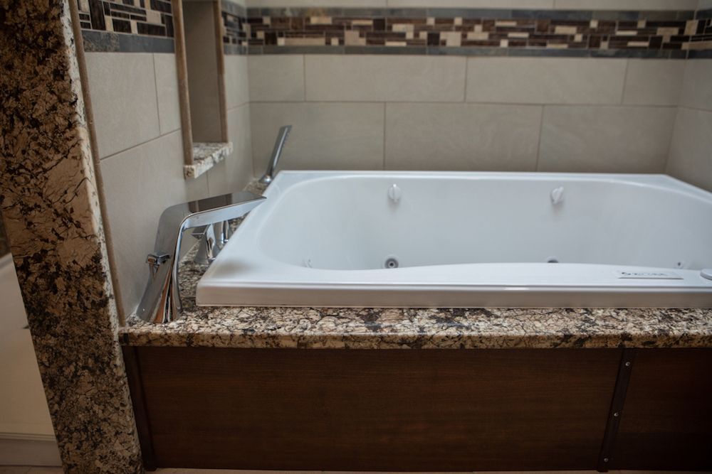 White jacuzzi tub with chrome fixtures in a bathroom, with a brown cabinet and granite trim.