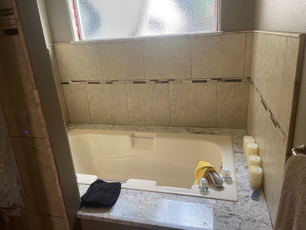 Bathroom with bathtub and partially tiled walls. Beige and brown tiles are featured, with a window above the tub.
