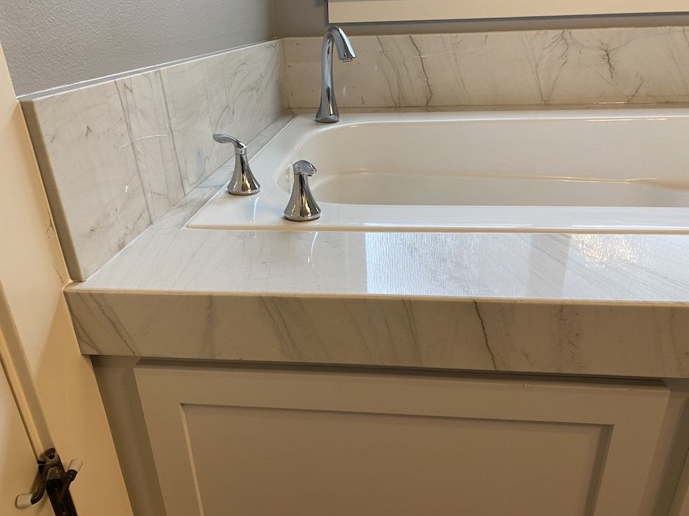 White marble-look countertop and tub surround with chrome faucet and fixtures.