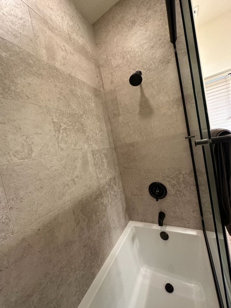 Bathroom with gray tiled walls, black shower fixtures, and a white bathtub.