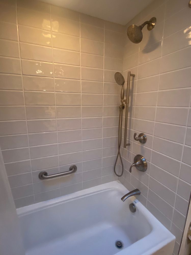 Bathtub with tiled walls, showerhead, and grab bar.