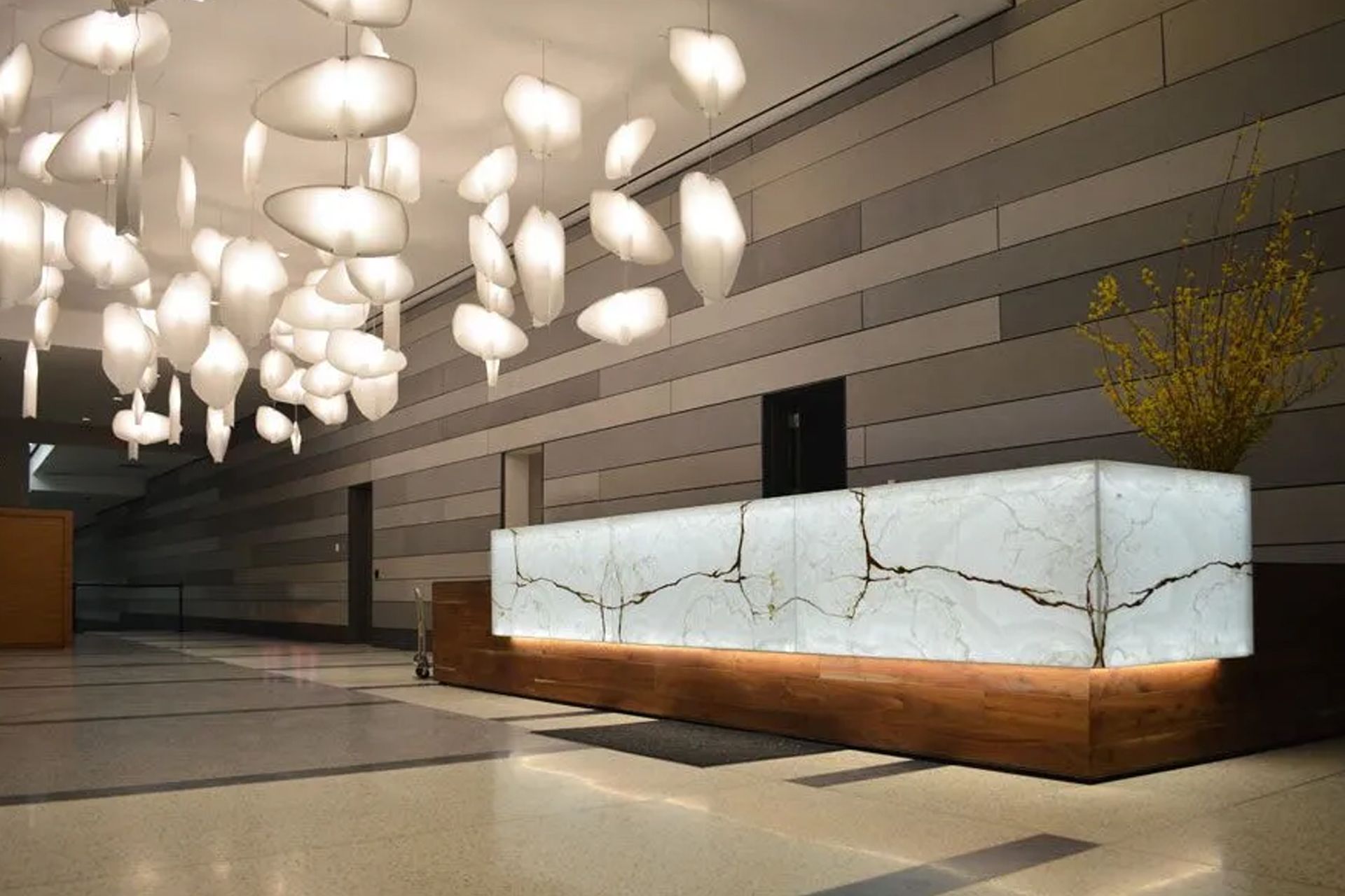 Modern hotel lobby with illuminated white reception desk, wood base, and abstract light fixture.