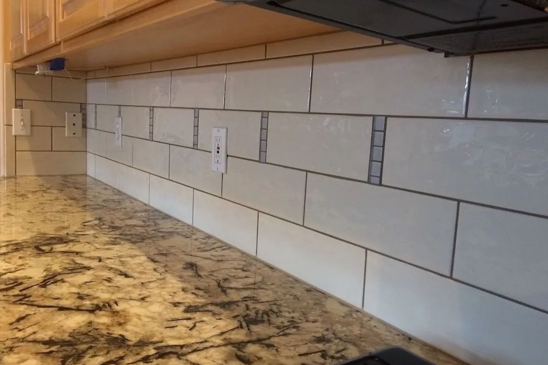 White subway tile backsplash installed above a granite countertop in a kitchen.