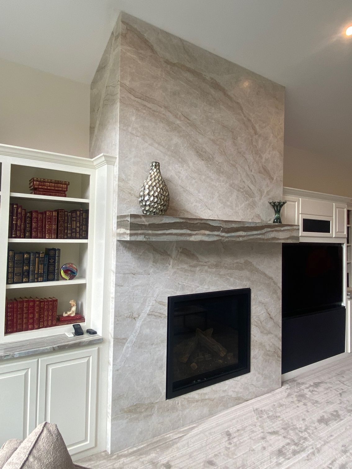 Stone-surrounded fireplace with black insert, flanked by white built-in bookshelves and a TV, tan and grey color scheme.