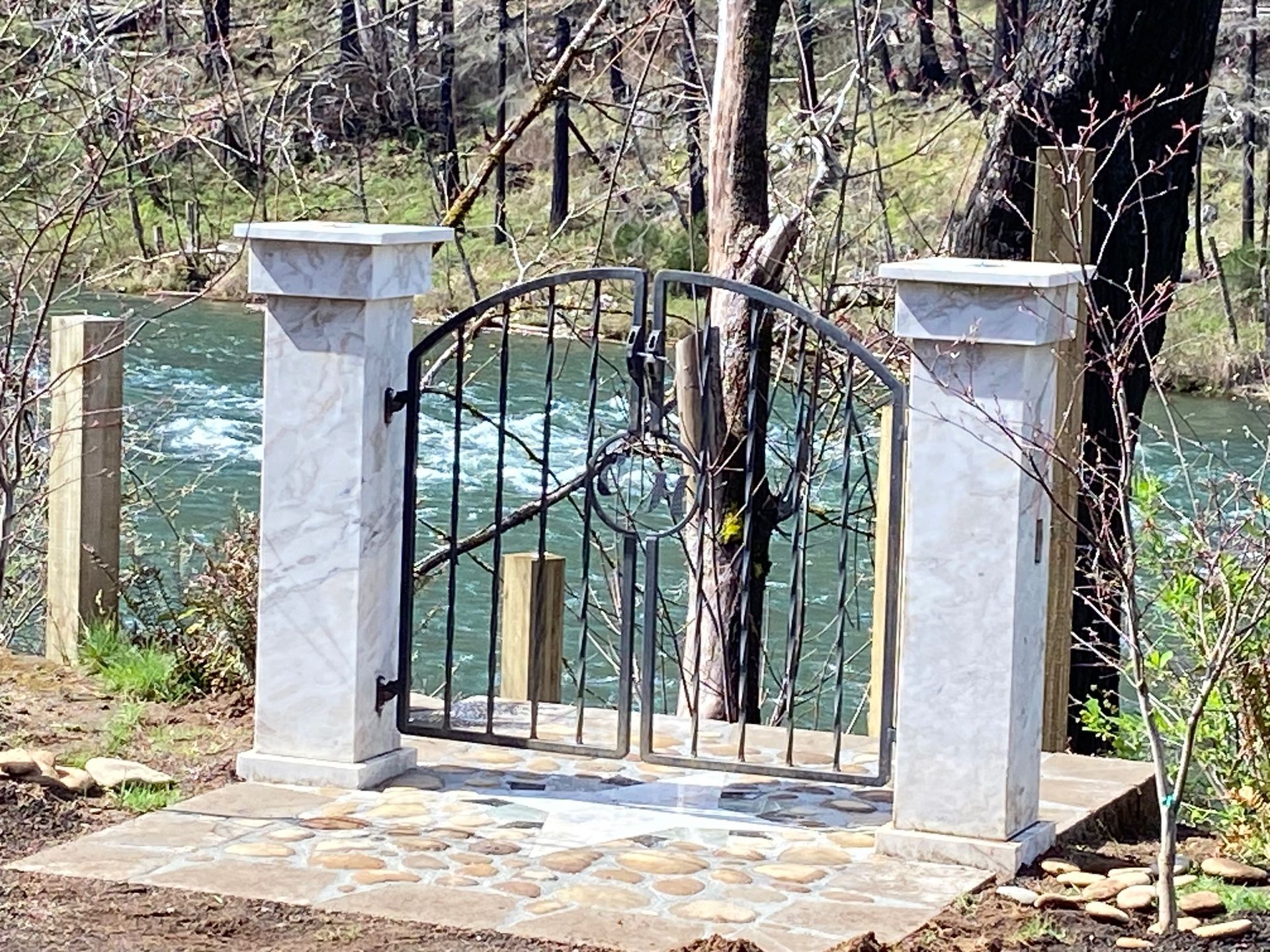 Metal gate between two stone pillars, leading to a river.