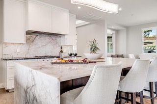 Modern white kitchen with marble countertops and island, bar stools, wine, and charcuterie board.