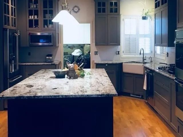 Kitchen with granite island, grey cabinets, stainless steel appliances, and wooden floor.