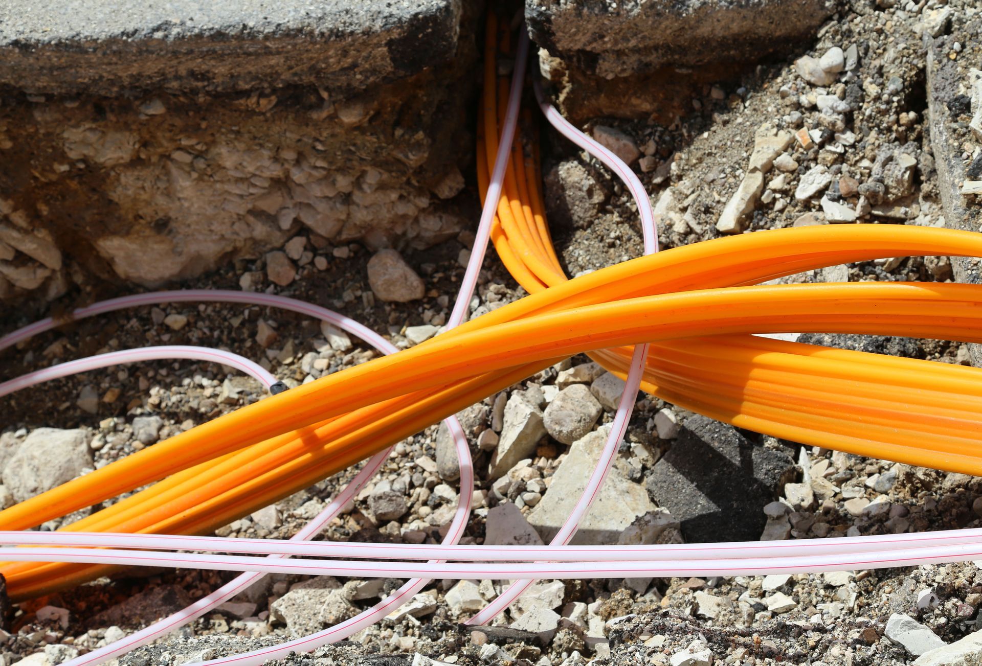 Orange and white cables running through a trench in rubble beside a brick wall