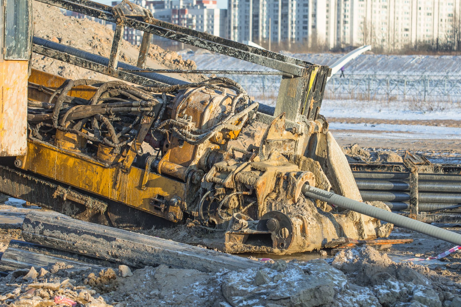 A yellow horizontal directional drilling machine operates in a muddy, snowy construction site.