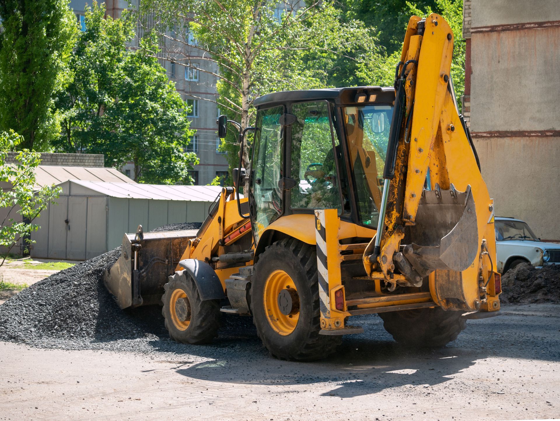 Yellow backhoe loader dumping gravel at a construction site outdoors