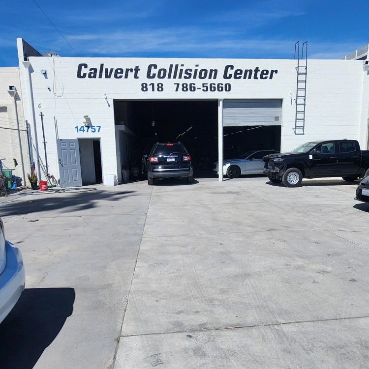 Calvert Collision Center with cars parked inside and outside the garage on a sunny day.