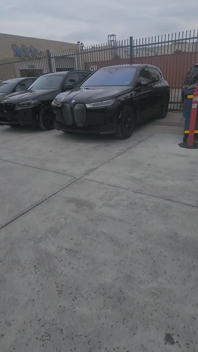 Black BMW SUV parked on concrete lot, cloudy sky in background.