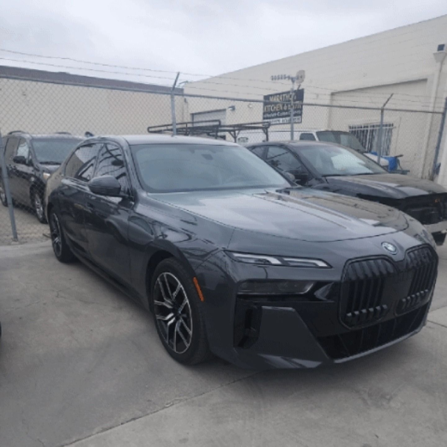 Dark gray BMW 7 series sedan parked outside a building, in an auto shop setting.