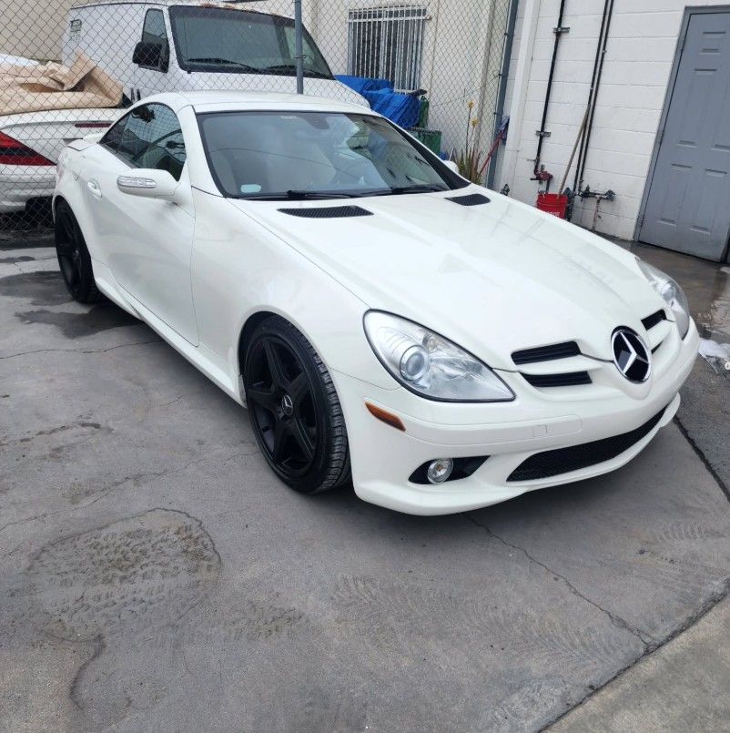 White Mercedes-Benz SLK-Class sports car with black rims parked outdoors on a concrete surface.