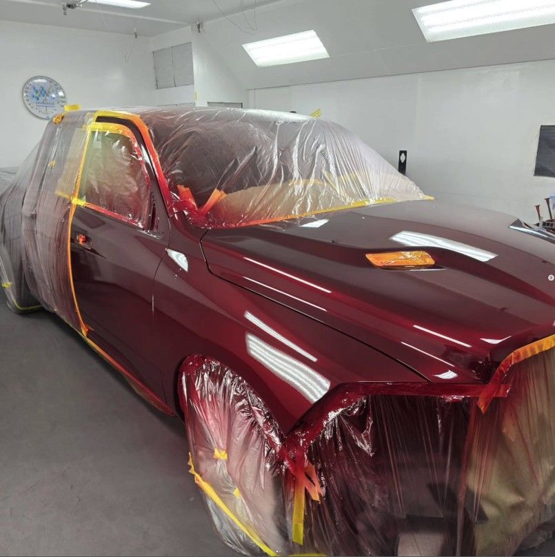 Maroon truck in a paint booth, covered in plastic and tape, ready for painting.